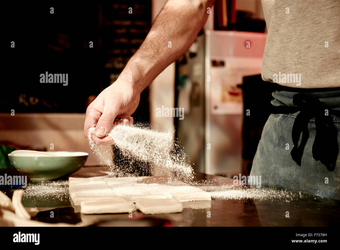 Un panadero trabaja sobre una superficie enharinada, dividiendo la masa preparada en forma de cuadrados. Foto de stock