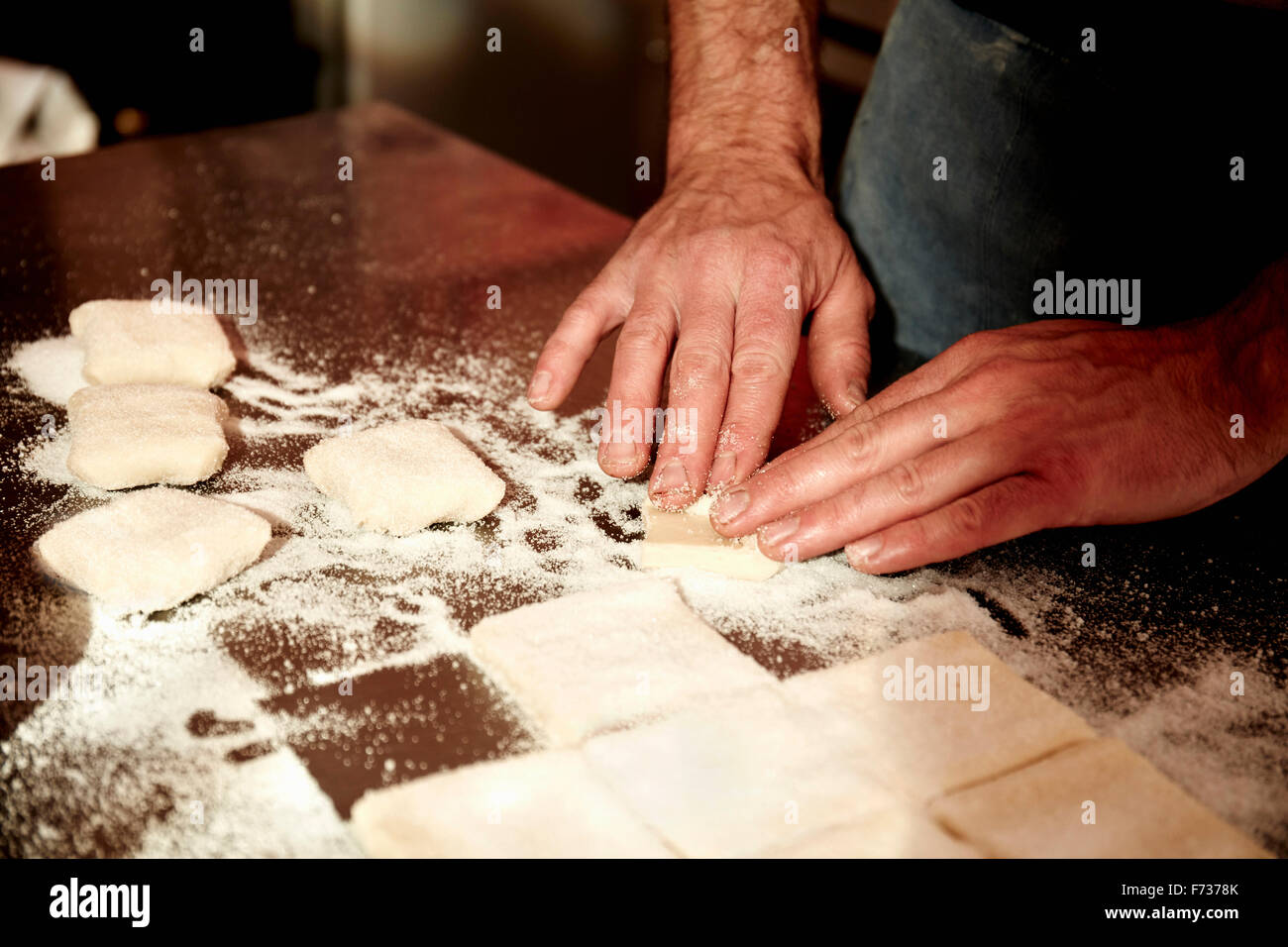 Un panadero trabaja sobre una superficie enharinada, dividiendo la masa preparada en forma de cuadrados. Foto de stock