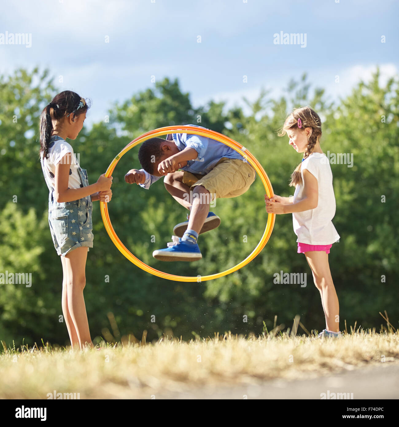 Niños jugando en un parque infantil con una niña haciendo hula hoop con una  chaqueta naranja fotos de archivo