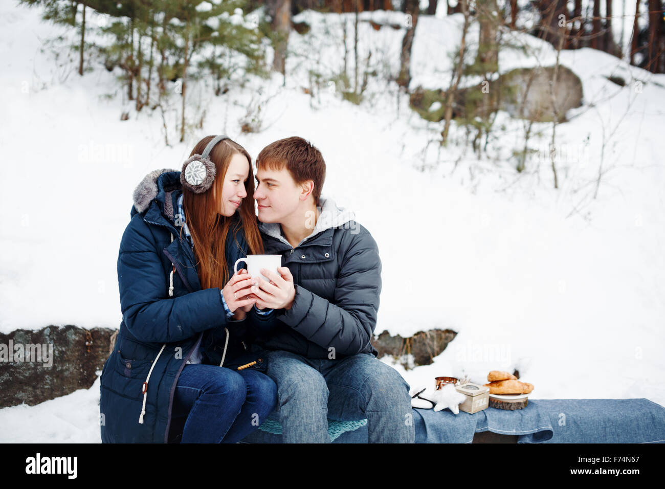Feliz pareja sentados al aire libre en invierno bosque beber bebida caliente y Mirarse Foto de stock