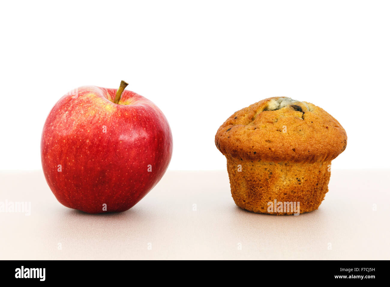 Rosy manzana roja comida sana opción y un muffin pastel snack insalubre sobre una mesa para ilustrar los alimentos alternativos de salud el concepto de elección. Inglaterra Foto de stock