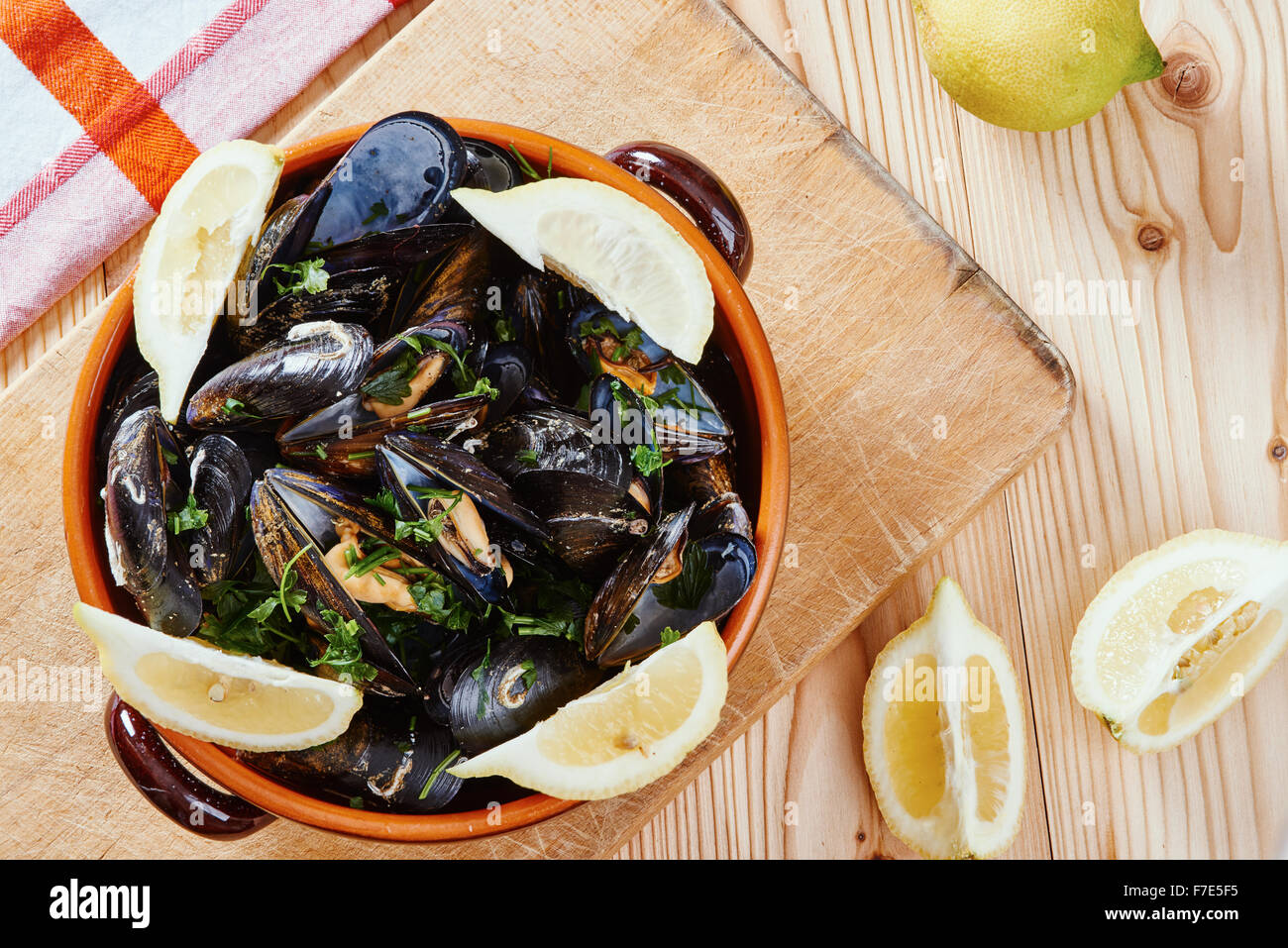 Los mejillones en una olla sobre la placa de corte, limones, mantel sobre mesa de madera Foto de stock