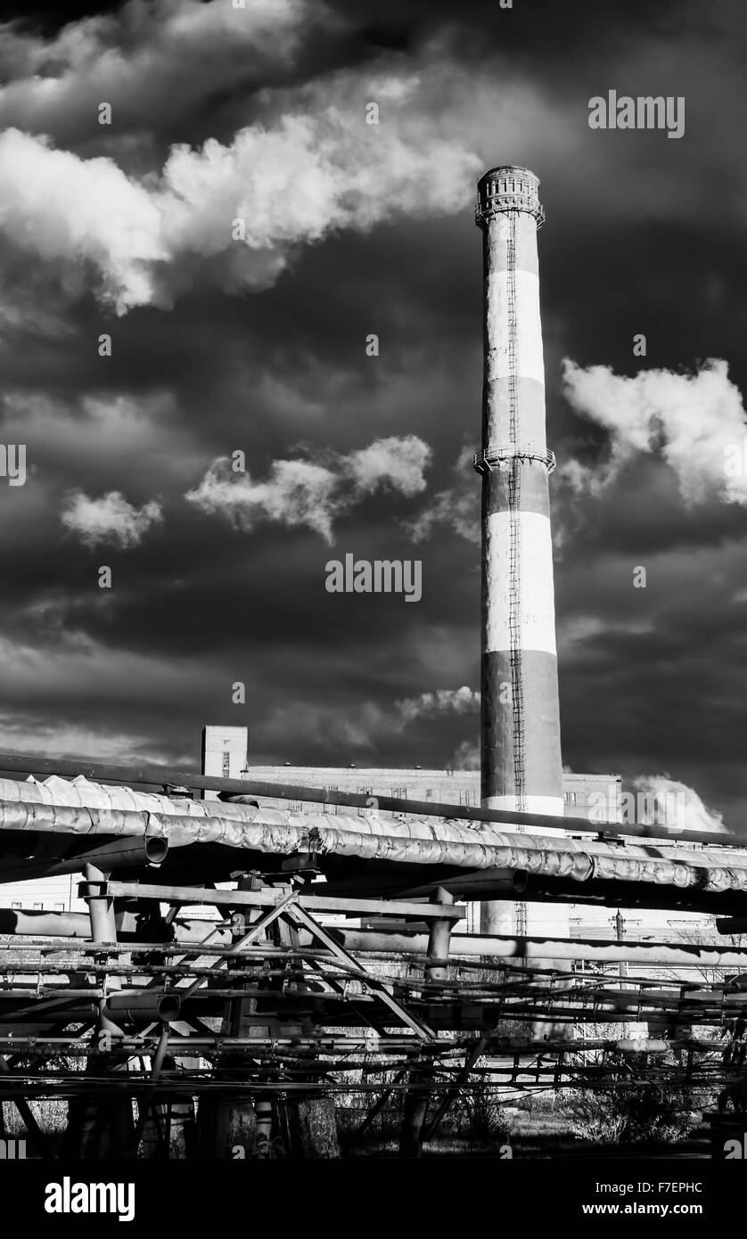 Fábrica enorme chimenea en blanco negro elevándose por encima hacia un cielo azul eructos enormes penachos de humo o contaminación en t Foto de stock