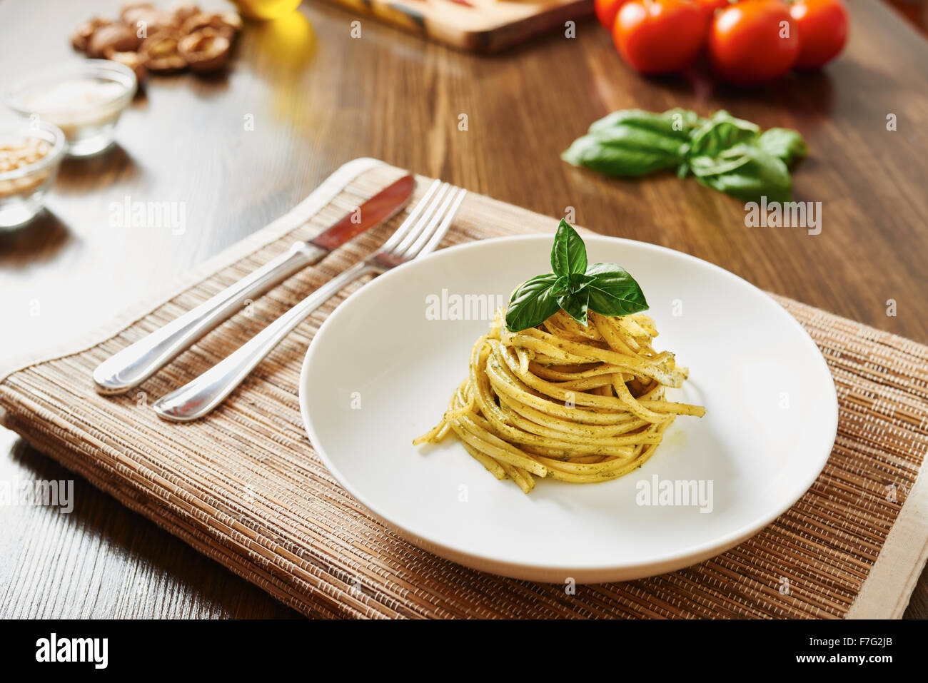 Pasta con salsa pesto sobre placa blanca rodeada por ingredientes, sobre mesa de madera Foto de stock