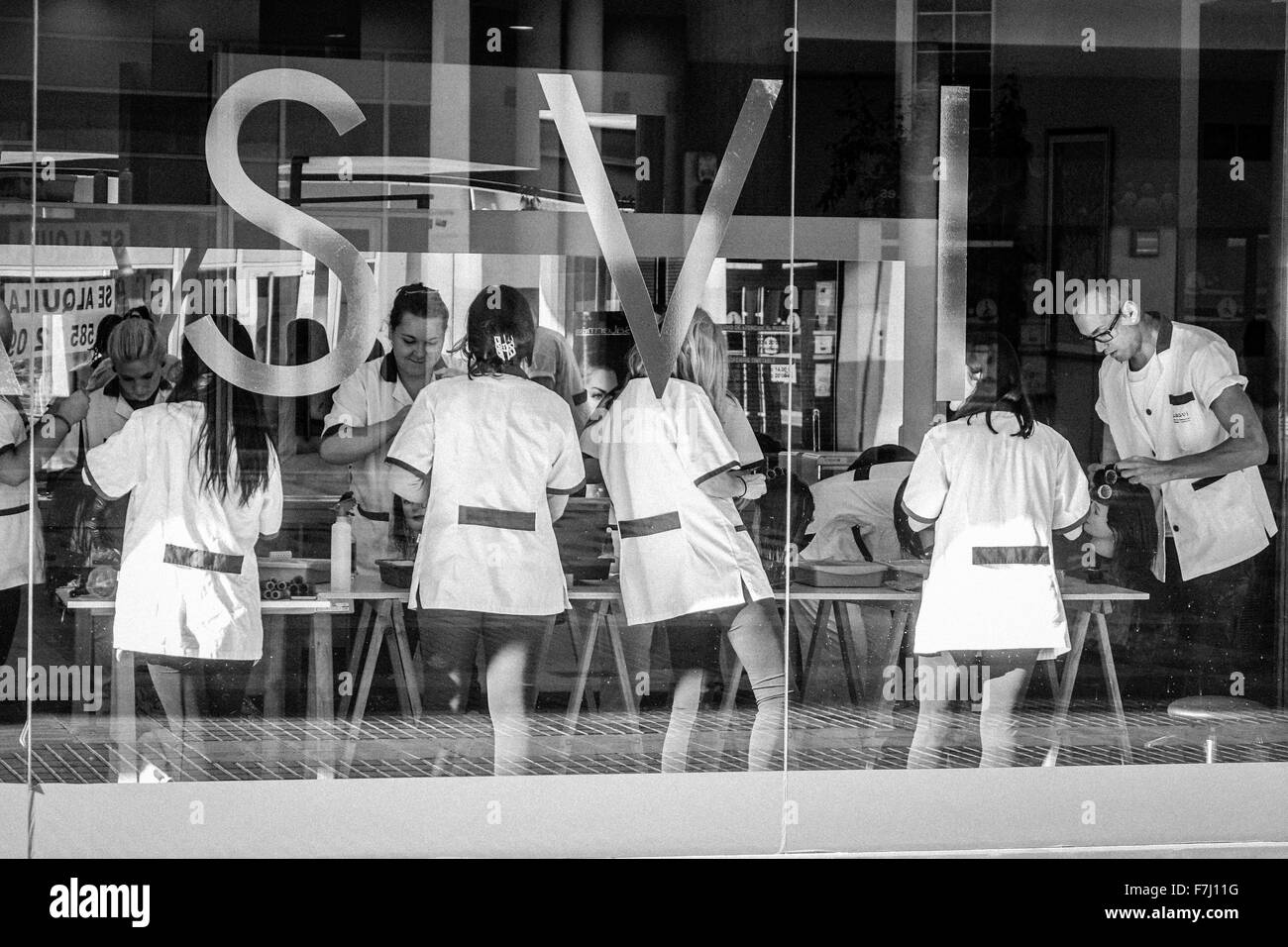 Benidorm, España, estudiante universitario de peluquería a los becarios que trabajan en clientes vistos a través de la ventana grande Foto de stock