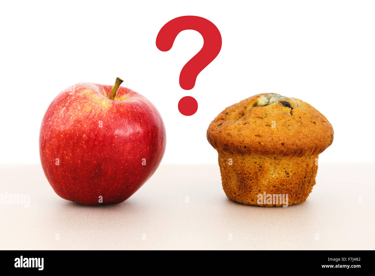 Rosy manzana roja y un muffin pastel sobre una mesa con un signo de interrogación entre para ilustrar las opciones de alimentos saludables y no saludables de concepto Foto de stock