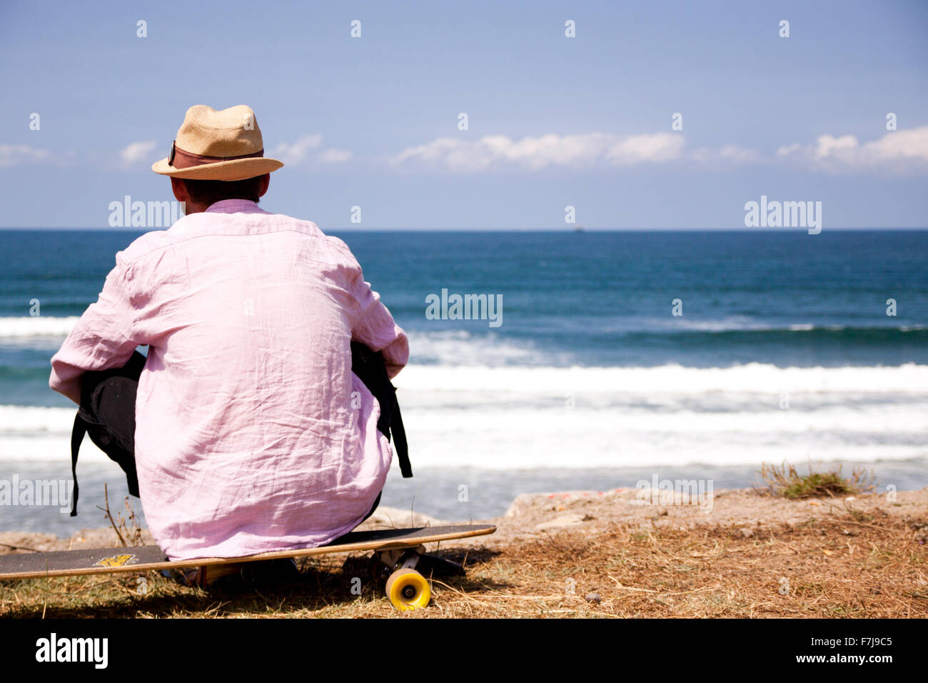Hombre mirando el mar y las olas desde la orilla sentado en su monopatín  Fotografía de stock - Alamy