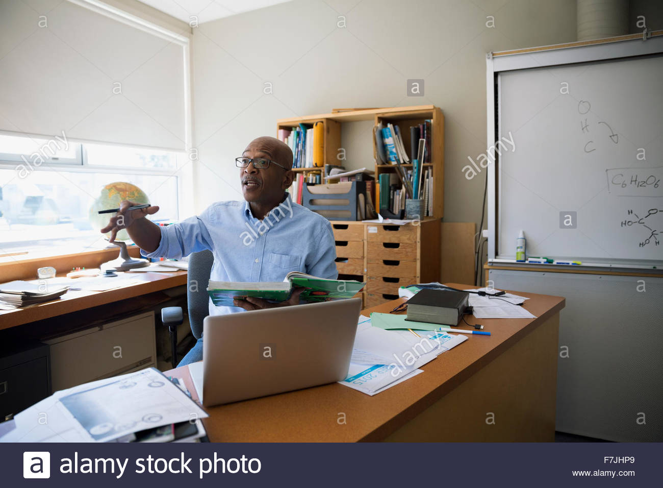 Profesor con gestos de libros de texto en el escritorio Foto de stock