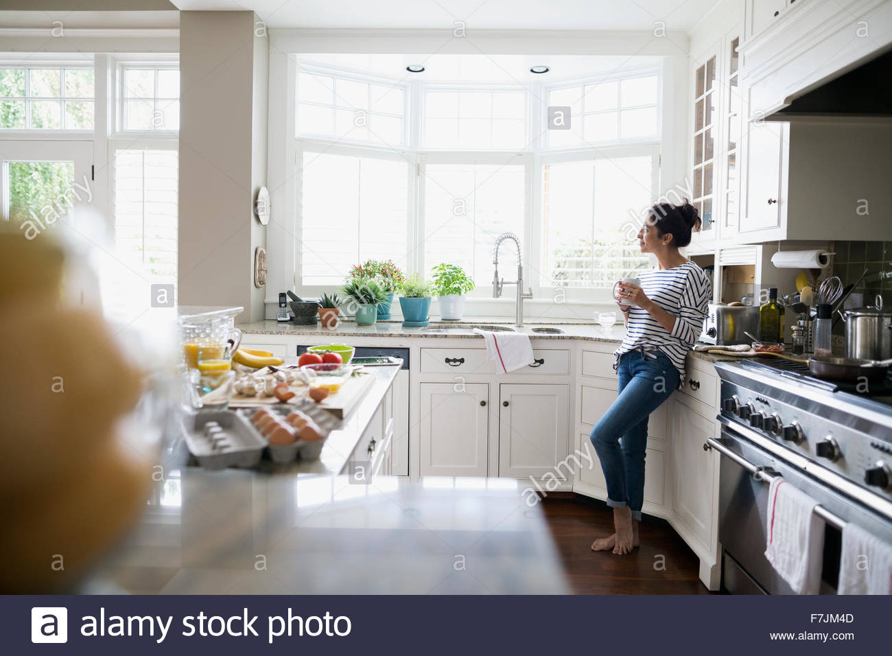 Mujer pensativa bebiendo café mirando por la ventana de la cocina Foto de stock