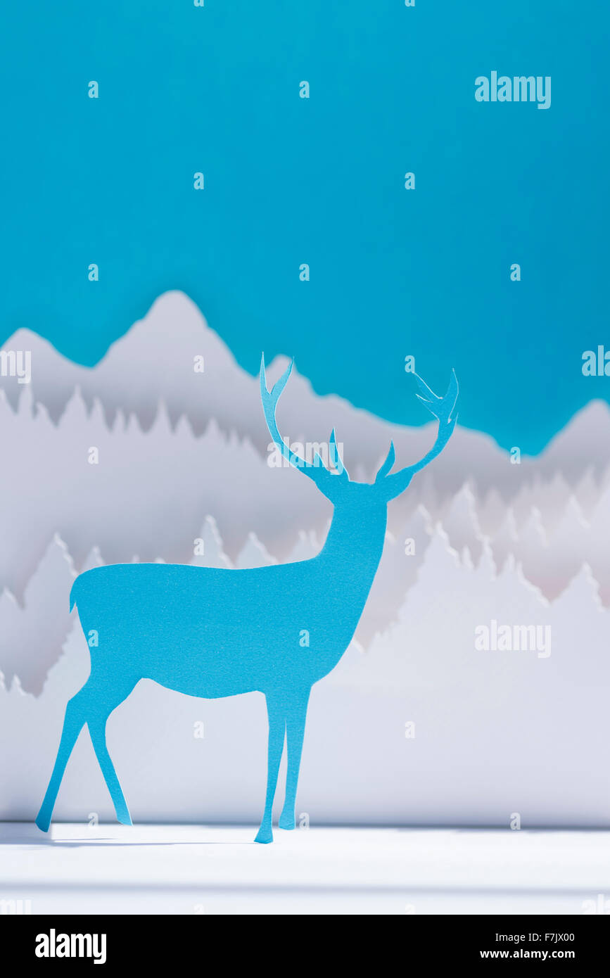 Holiday papel cortado renos en invierno bosque azul de fondo. Plantilla artesanal ideal para tarjetas de felicitación de Navidad, Año Nuevo Foto de stock