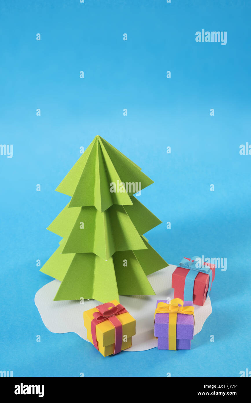 Árbol de Navidad en papel cortado estilo artesanal con cajas de regalo en color sobre fondo azul. Ideal para vacaciones de Navidad, Tarjetas de felicitación Foto de stock
