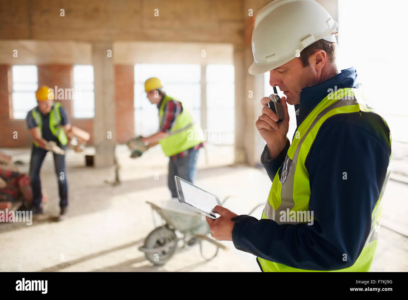 Capataz con tableta digital utilizando un walkie-talkie en sitio en construcción Foto de stock