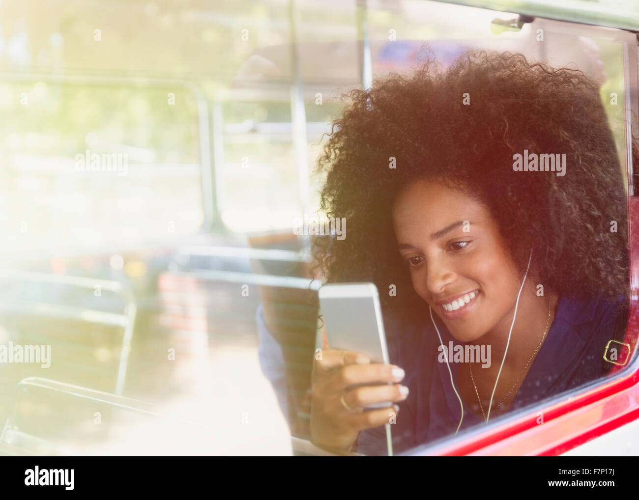 Mujer sonriente con afro, escuchar música con auriculares y reproductor de mp3 en bus. Foto de stock