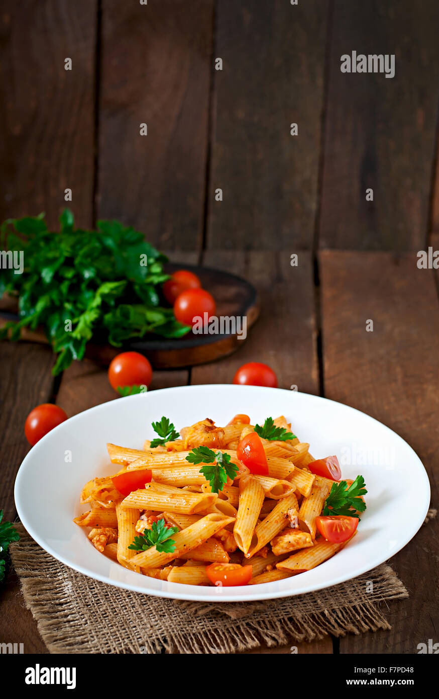 Pasta Penne con pollo en salsa de tomate, los tomates están decoradas con perejil en una mesa de madera Foto de stock