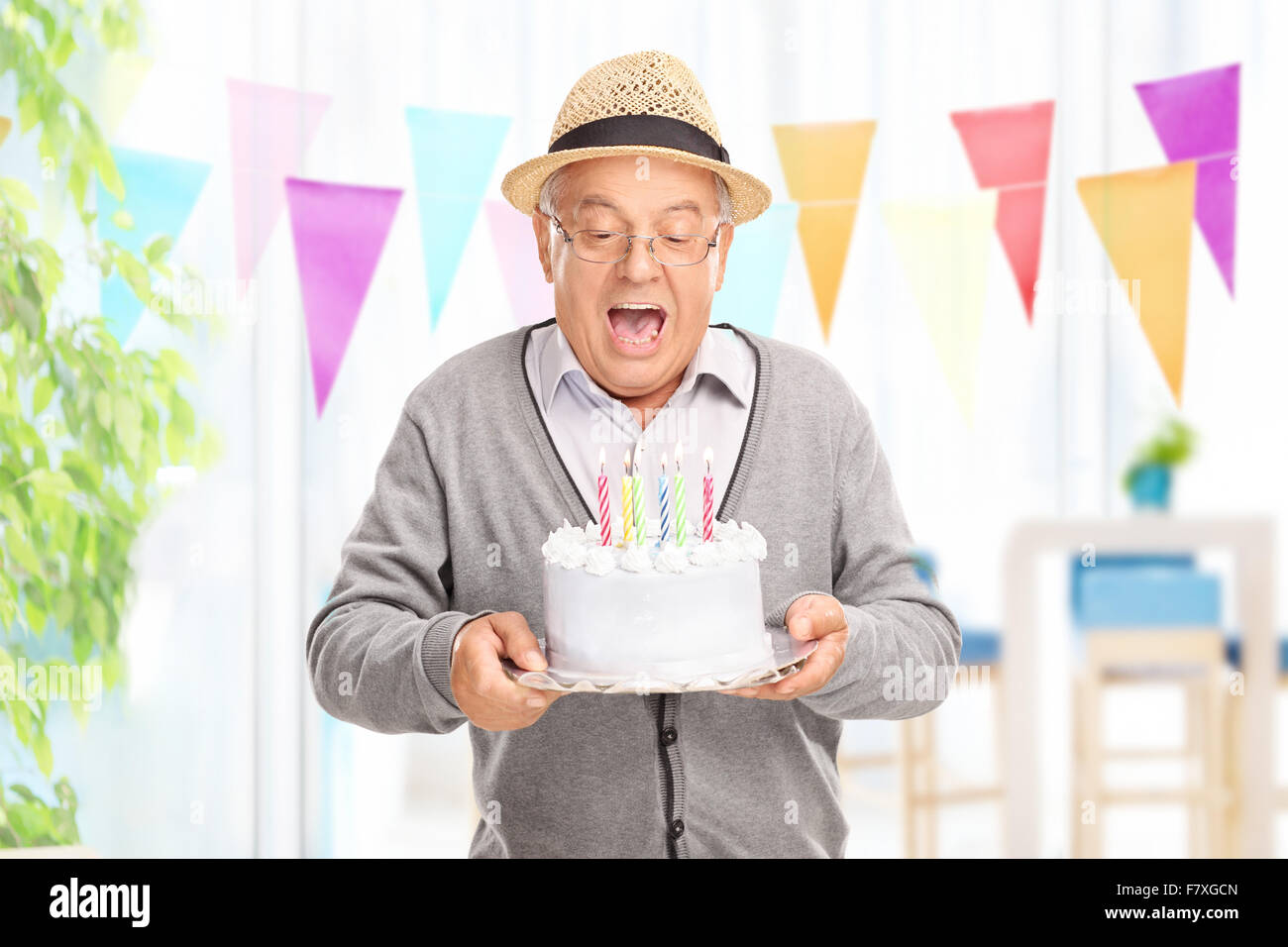 Encantado caballero senior soplando las velas en su pastel de cumpleaños en casa Foto de stock