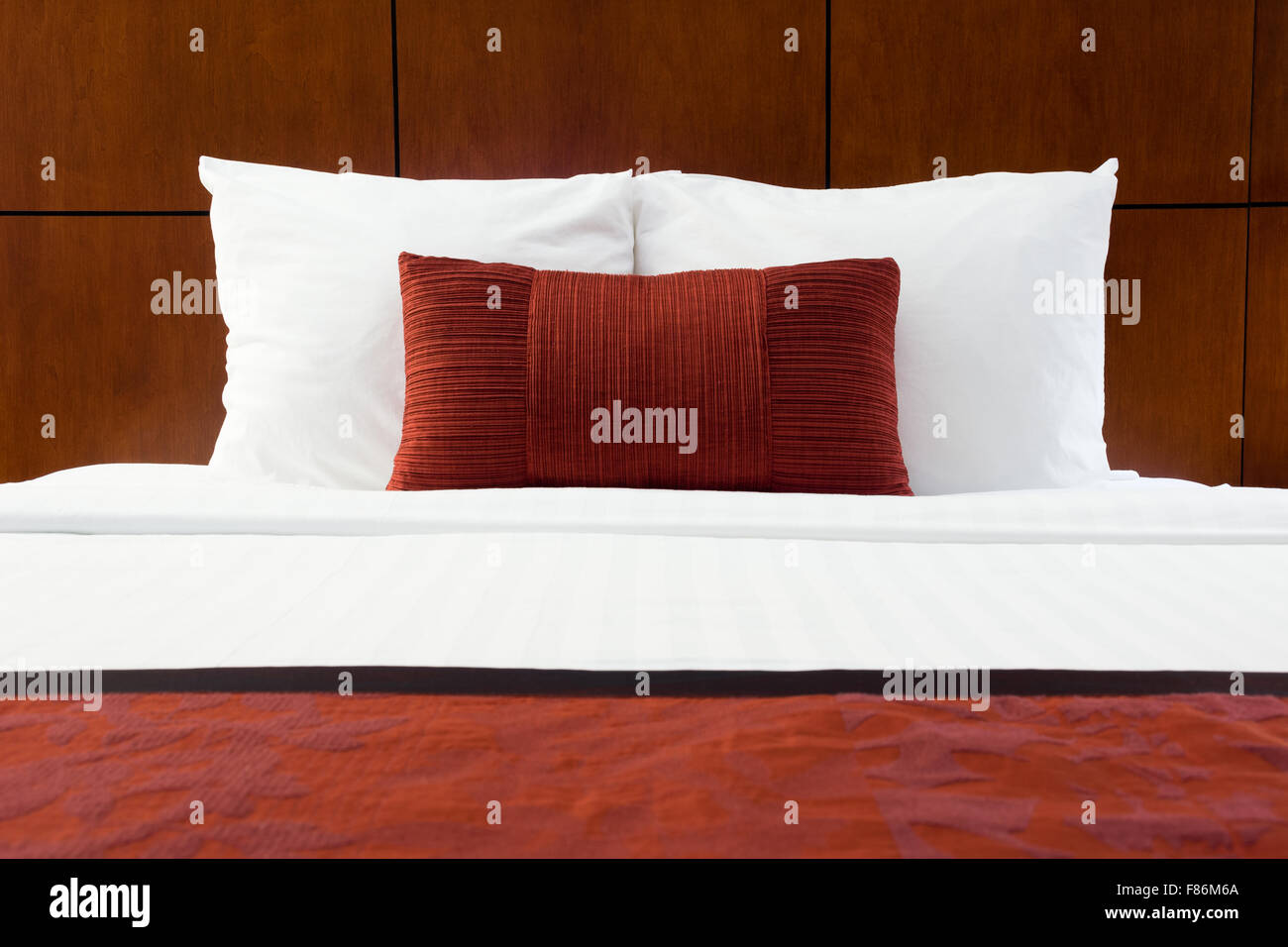 Habitación cama, almohadas, rojo y cabecero de madera en un hotel de lujo Foto de stock