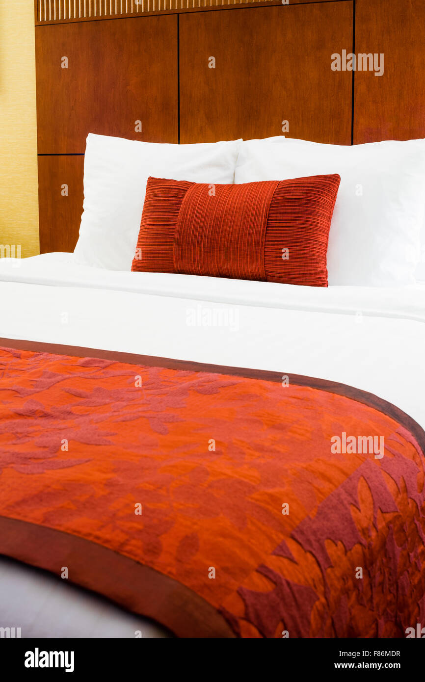 Habitación de hotel con cama con edredón y almohada de color borgoña. Foto de stock