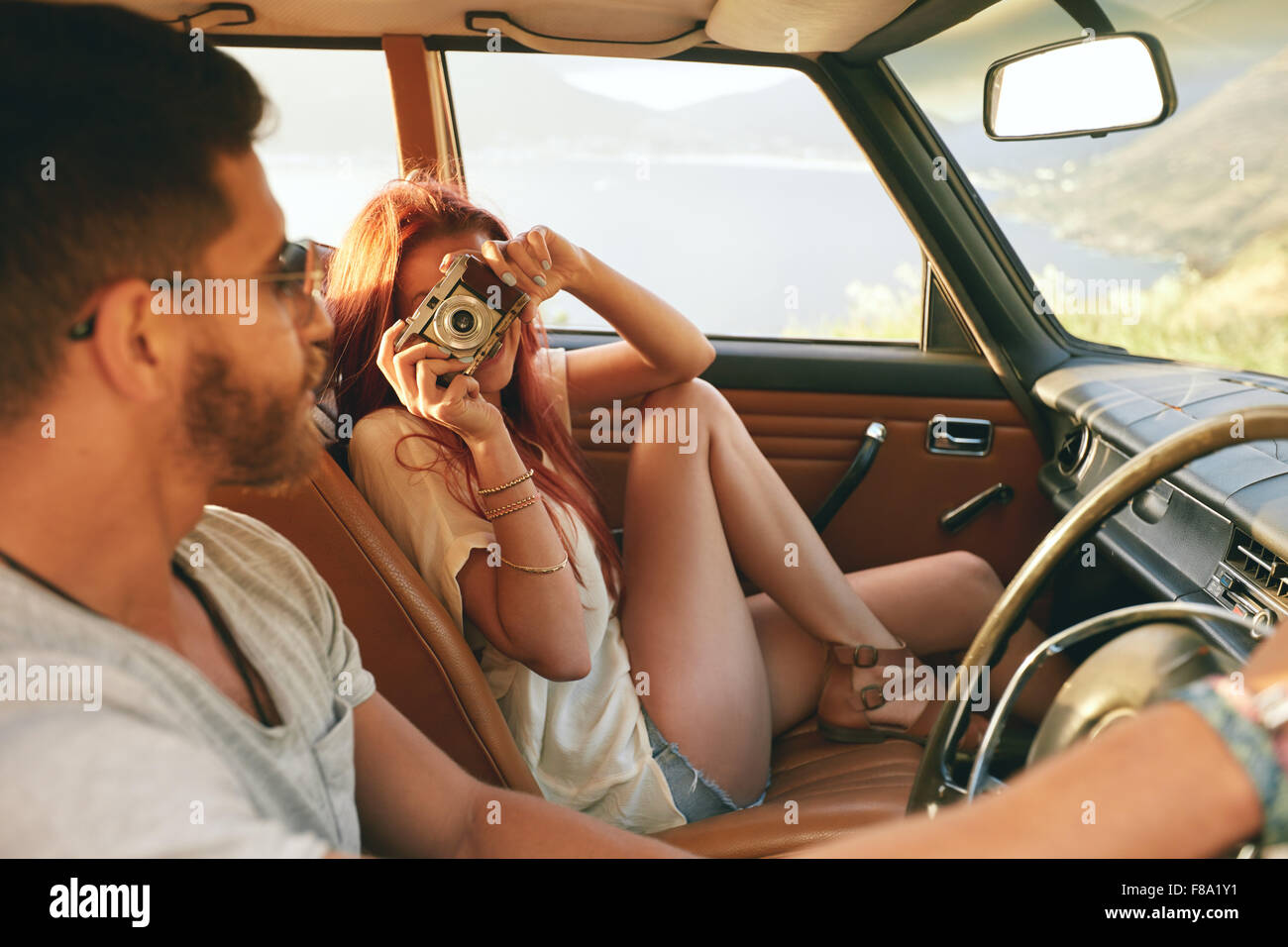 Caucasian par ir en un viaje por carretera. Mujer toma fotografías con la cámara y el hombre la conducción de automóviles. Foto de stock