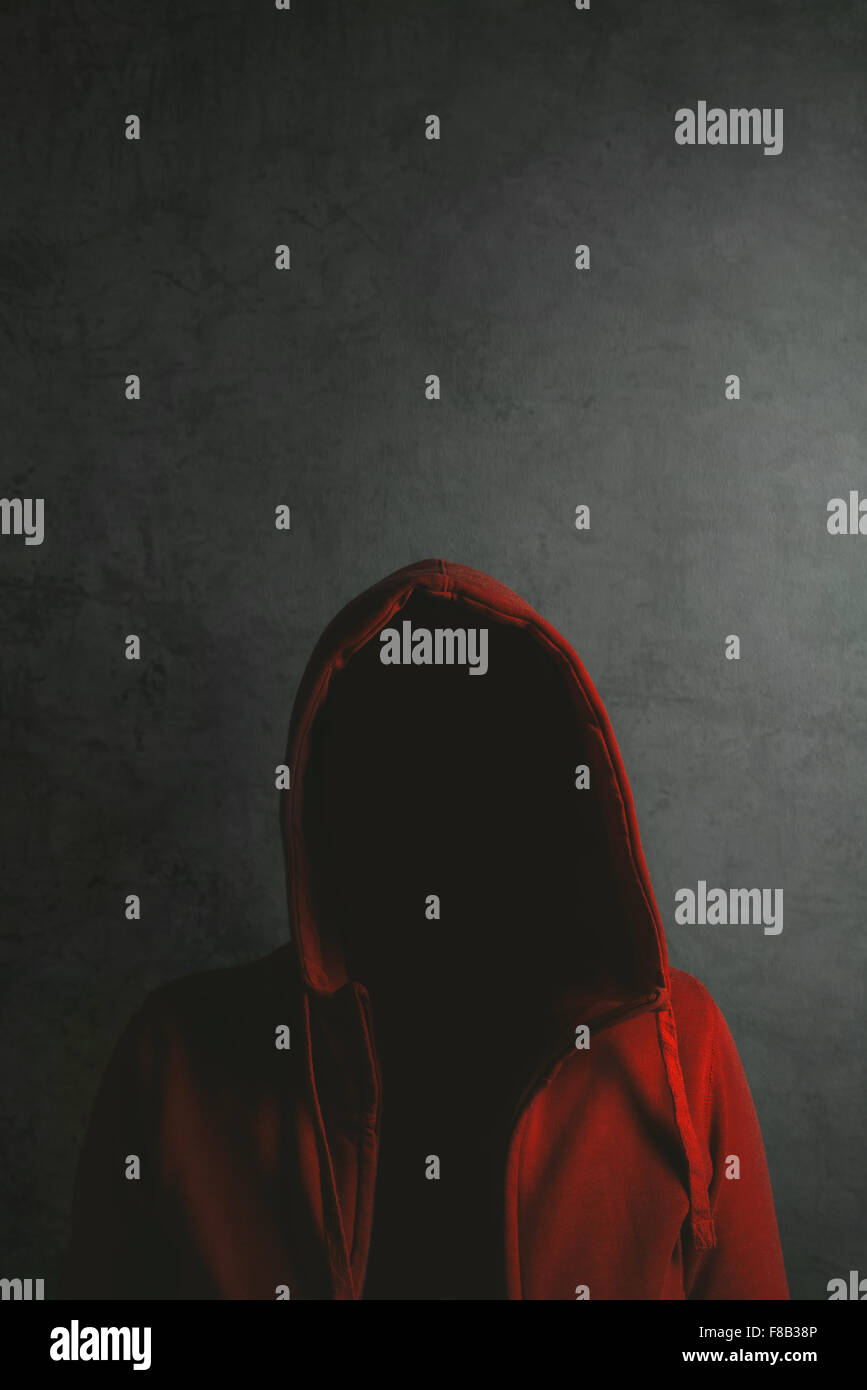 Persona irreconocible vistiendo la camiseta con capucha roja, bajo llave en una habitación oscura vertical Foto de stock