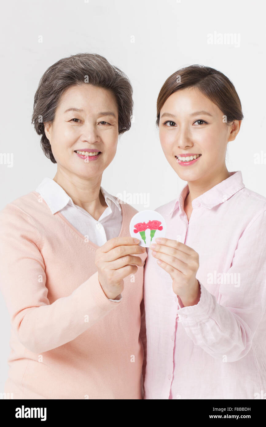 Madre e hija adulta sostiene una fotografía de clavel juntos y sonrientes Foto de stock