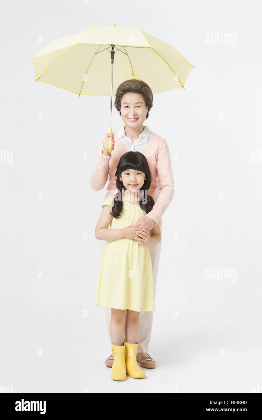 Abuela sosteniendo paraguas con su nieta vistiendo vestido amarillo y amarillo, botas de agua Foto de stock