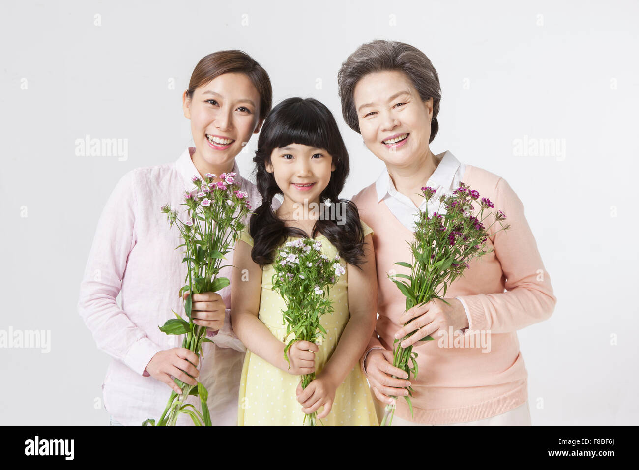 Adulto joven mujer, niña y mujer senior todos sosteniendo flores y mirando hacia adelante con una sonrisa Foto de stock