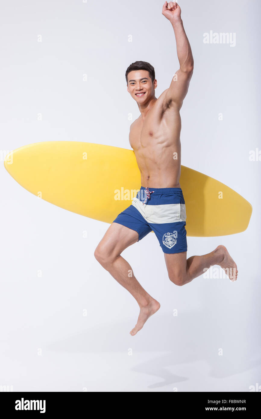 El hombre muscular la celebración de una junta de surf bajo el brazo y saltar con su mano alta Foto de stock