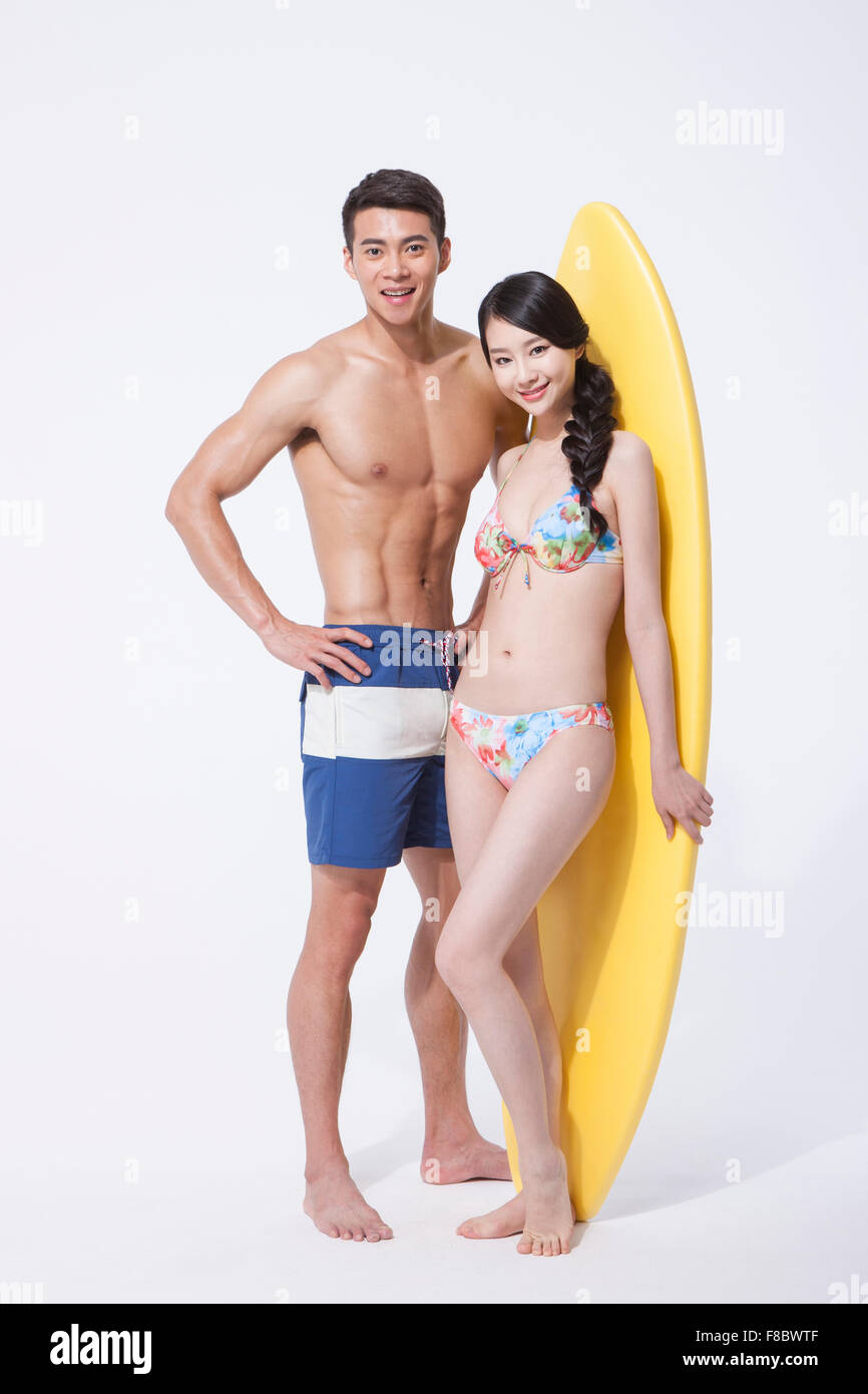 Muscular de un hombre y una mujer en traje de baño de pie y mirando hacia adelante con una junta de surf y la sonrisa permanente Foto de stock