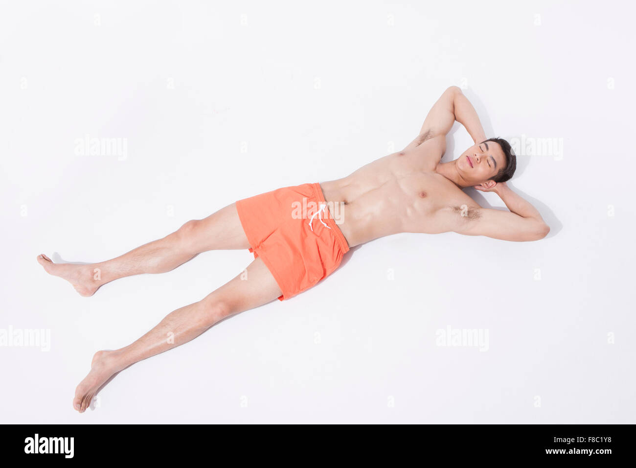 El hombre muscular en natación pantalones acostado con las manos en la parte posterior de la cabeza con los ojos cerrados Foto de stock