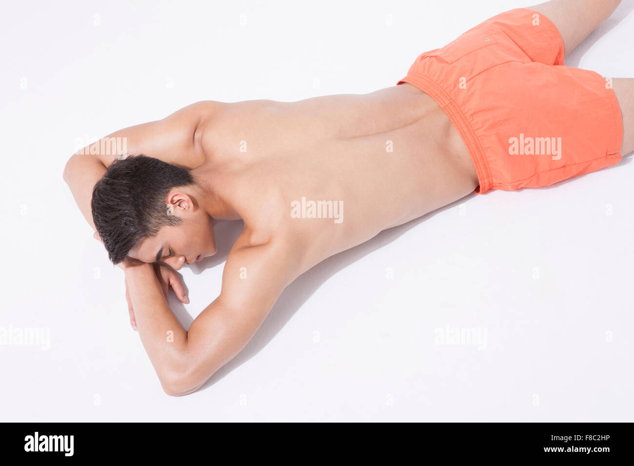 Alto ángulo de muscular en natación pantalones hombre tumbado en la parte delantera descansando su cabeza en sus manos con los ojos cerrados Foto de stock