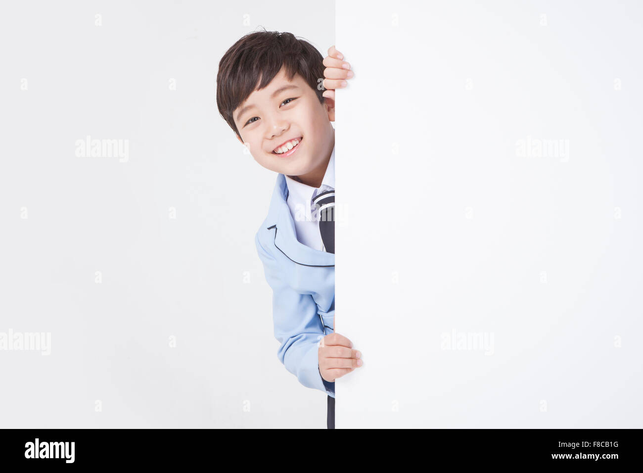 Niño en edad escolar uniformes escolares escondiéndose detrás de un espacio de copia en blanco y sonriente Foto de stock