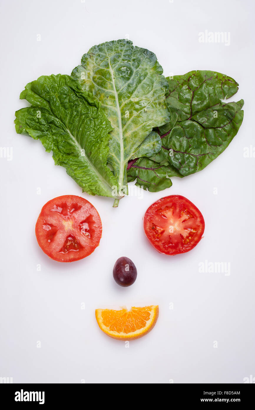 El arte de alimentos haciendo sonriente cara hecha con lechuga, rodajas de tomate, una uva, y una rodaja de naranja Foto de stock