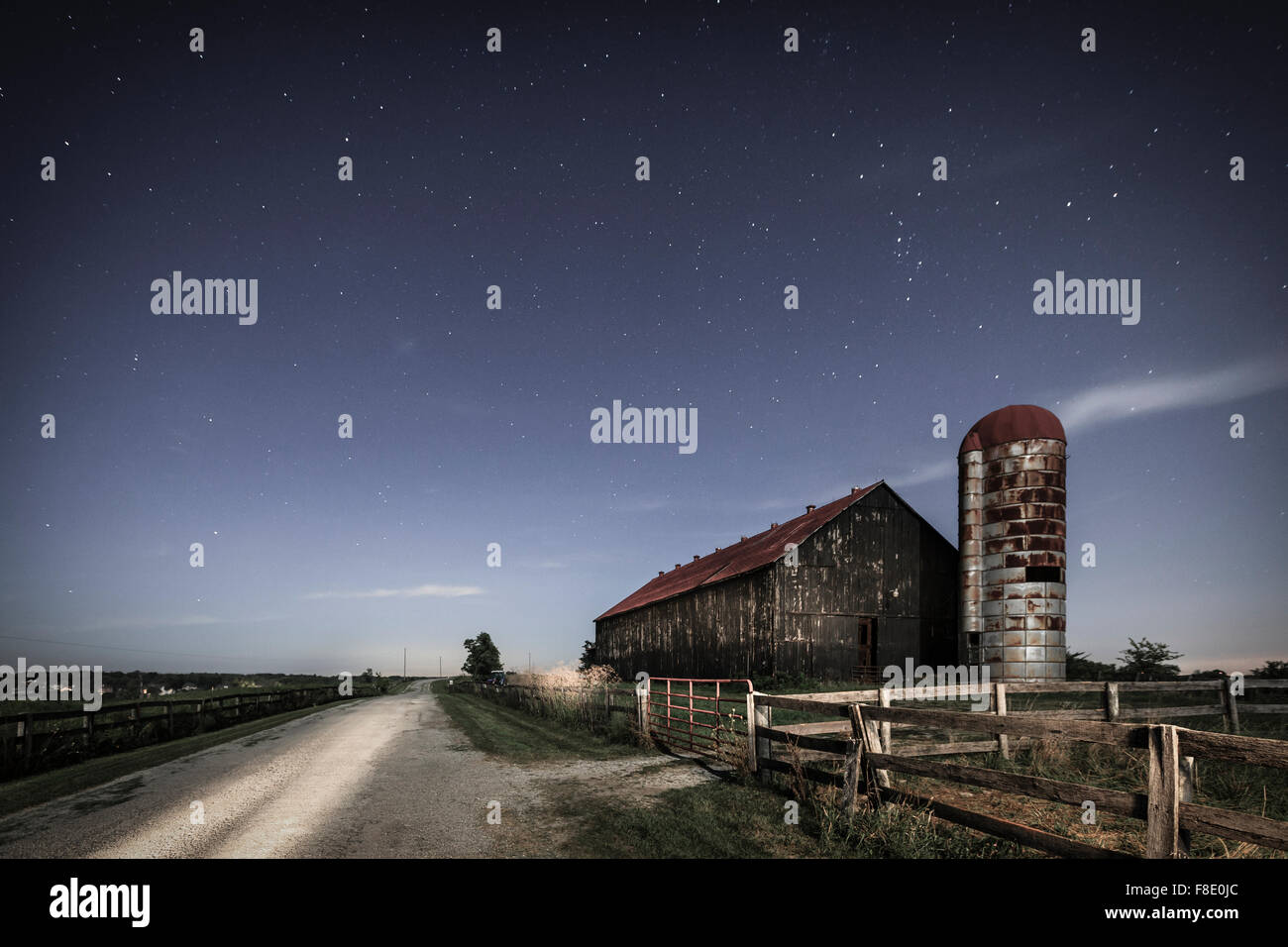 Imagen nocturna escénica de una antigua granja granero y un país por carretera en moonlight Foto de stock