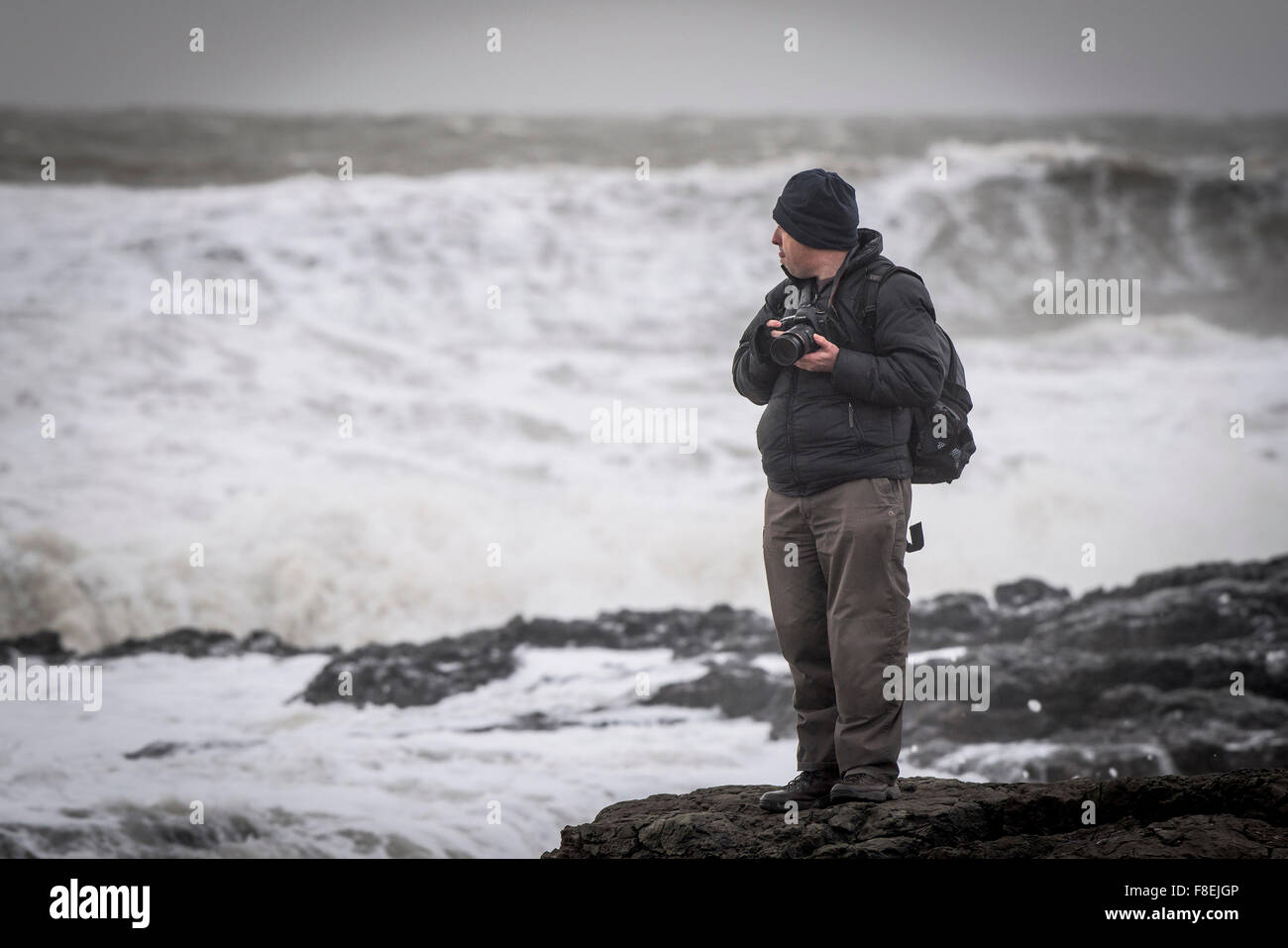 Un fotógrafo de pie sobre las rocas como el mar embravecido libra la costa en Porthcawl, Gales del Sur. Foto de stock