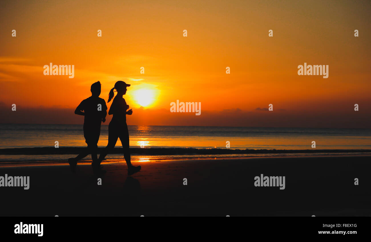 Pareja joven: hombre y mujer correr juntos en una puesta de sol sobre la costa del lago. Silueta. Foto de stock