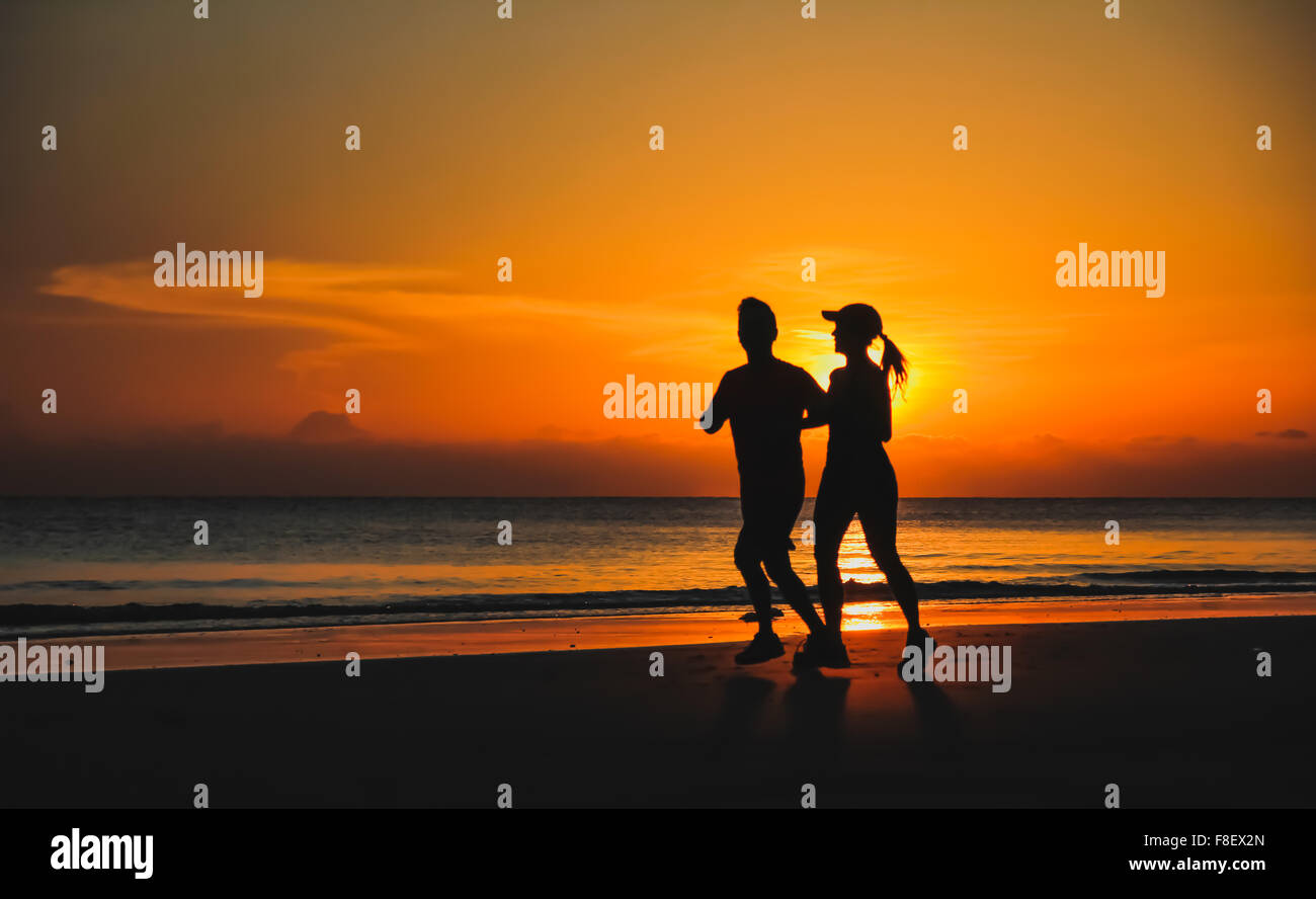 Pareja joven: hombre y mujer correr juntos en una puesta de sol sobre la costa del lago. Silueta. Foto de stock