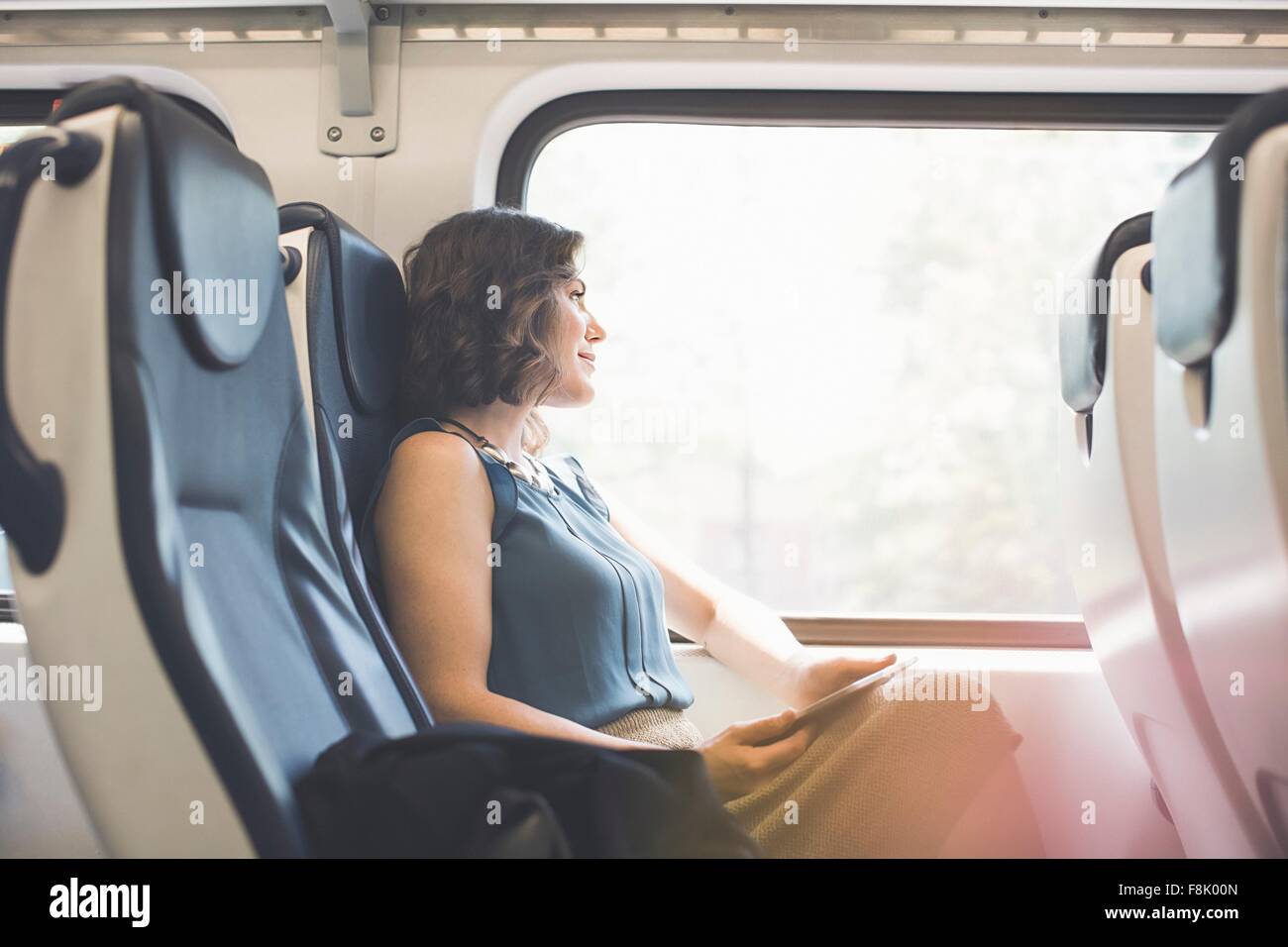 Mitad mujer adulta en el tren, la celebración de tableta digital, mirando afuera de la ventana Foto de stock