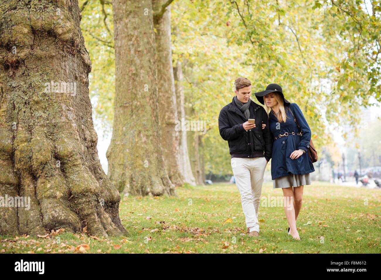Joven pareja romántica smartphone leer textos en Park, Londres, Inglaterra, Reino Unido. Foto de stock