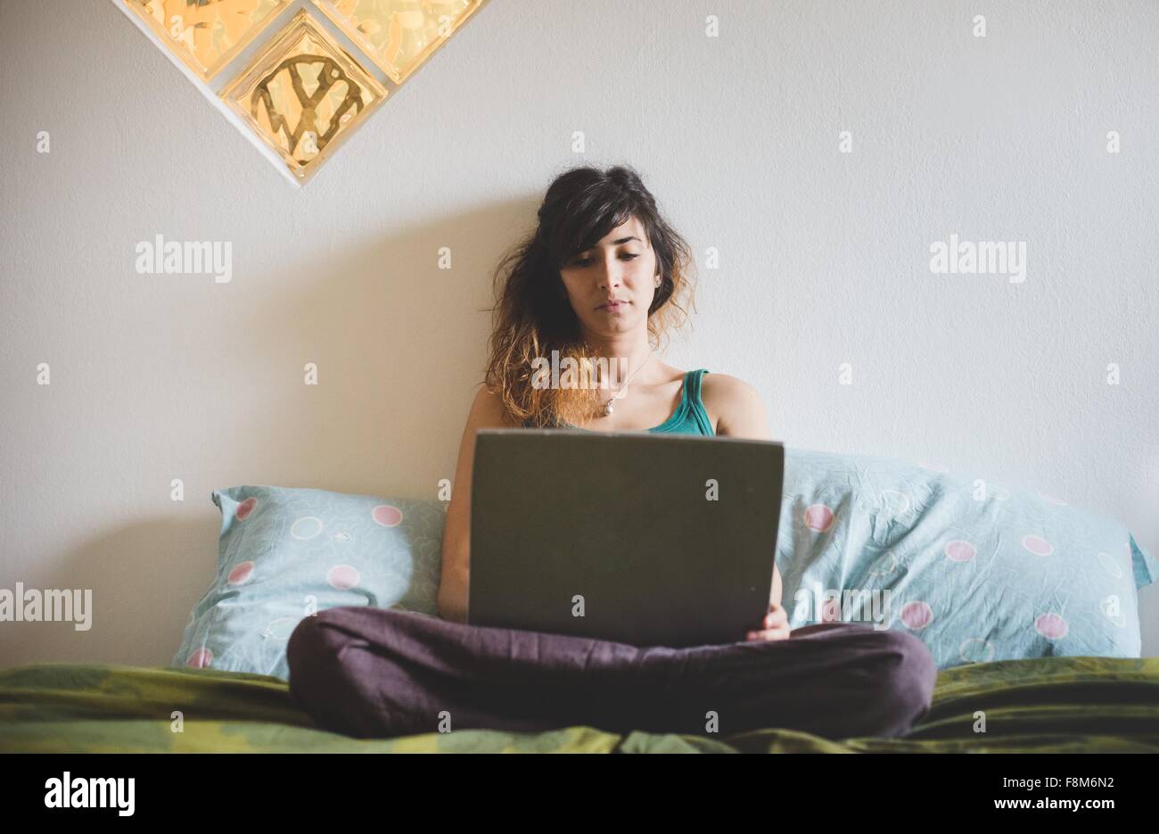 Vista frontal de la mujer adulta media piernas cruzadas sentado en la cama con ordenador portátil Foto de stock