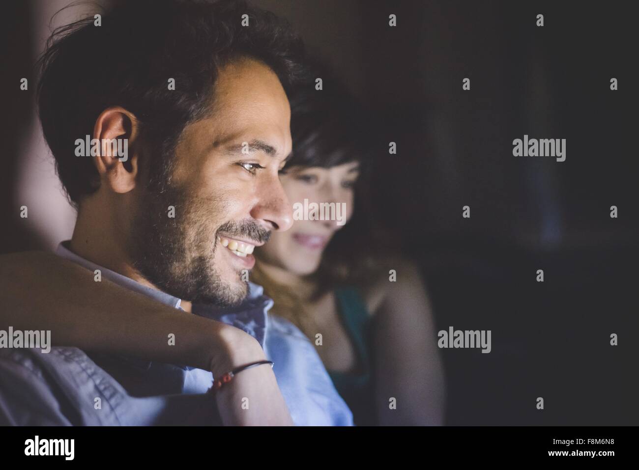 Vista lateral de la cabeza y los hombros de las jóvenes parejas iluminado en la pantalla de la computadora portátil sonriendo Foto de stock