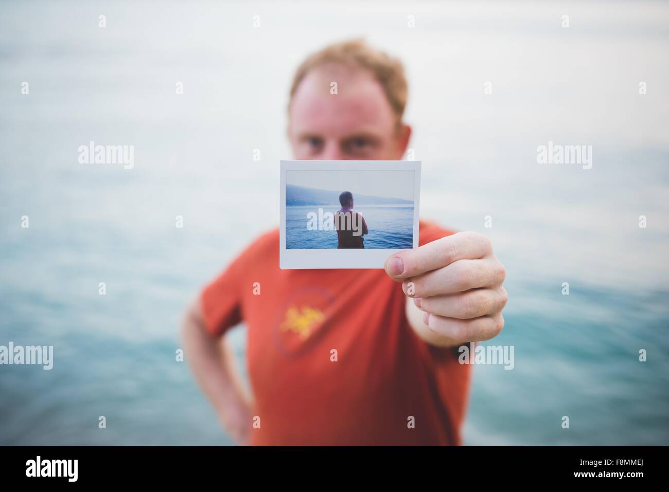 Hombre sujetando fotografía de sí mismo por el lago Foto de stock