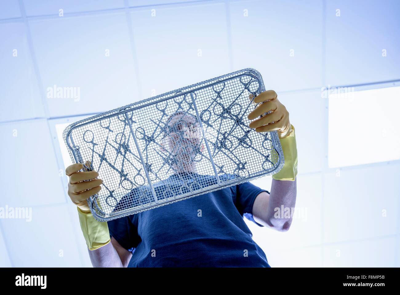 Trabajador con bandeja de instrumentos quirúrgicos en fábrica de instrumental quirúrgico, bajo ángulo de visión Foto de stock