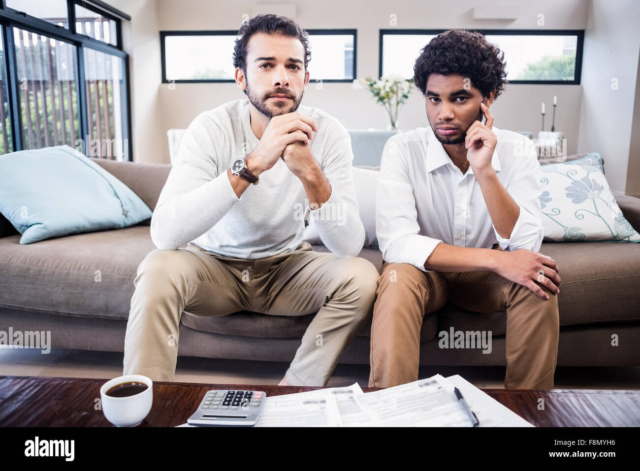 Preocupa una pareja gay con facturas en la mesa mirando a la cámara Foto de stock