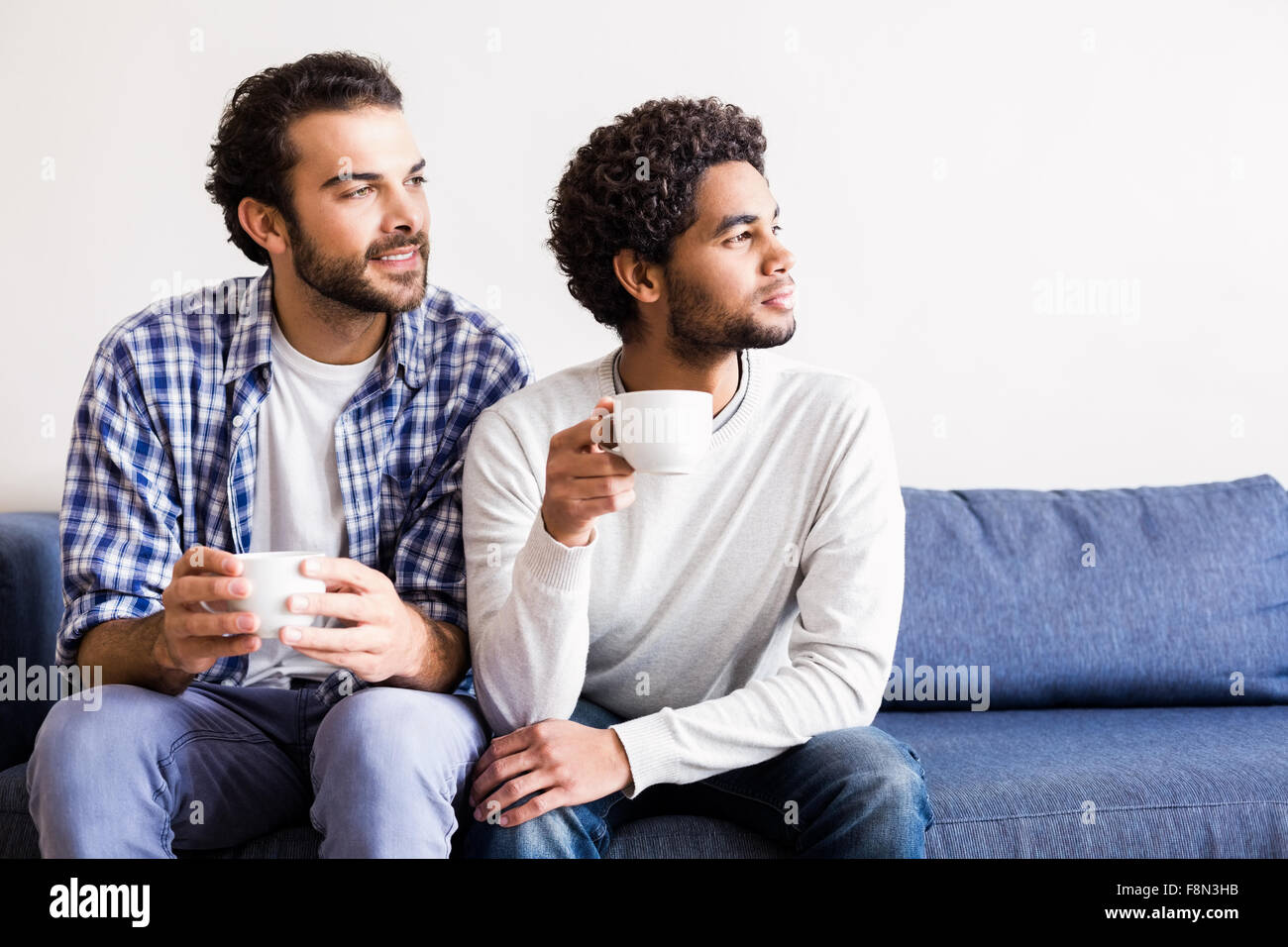 Una pareja gay sonriendo mirando lejos celebración blanco tazas Foto de stock