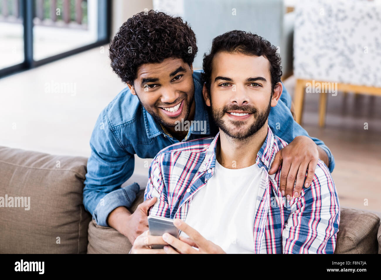 Feliz pareja gay utilizando el smartphone en el sofá Foto de stock