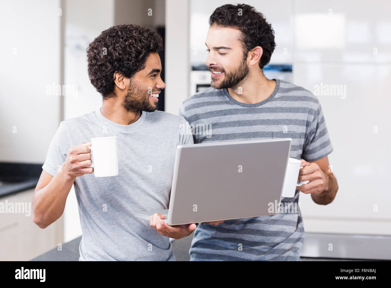 Feliz pareja gay con laptop y celebración tazas Foto de stock