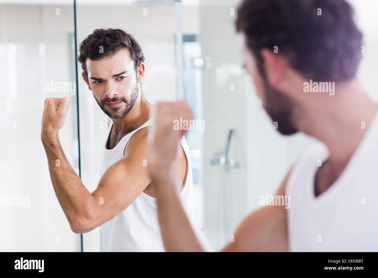 Hombre sonriendo mirando sus bíceps en espejo Foto de stock