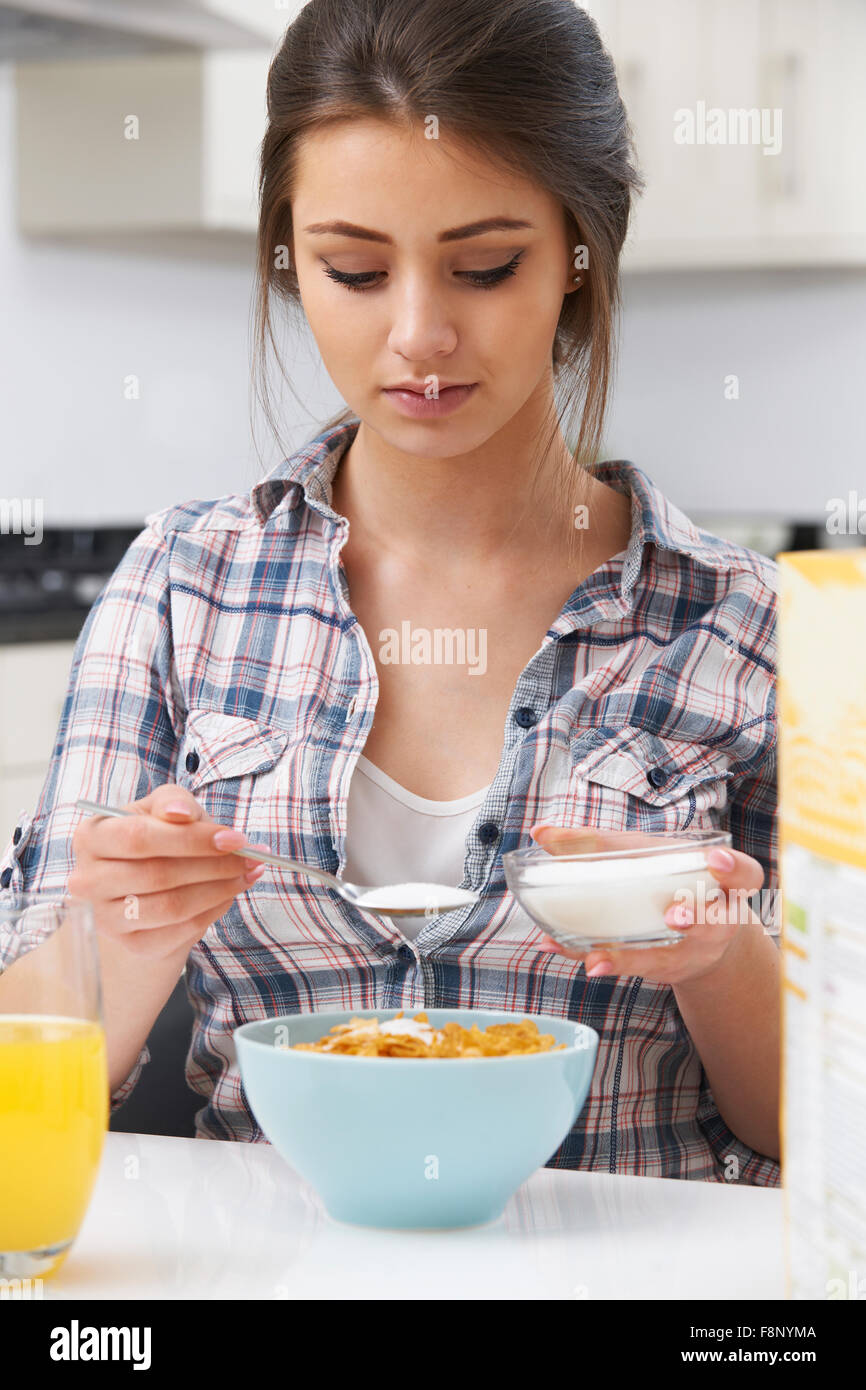 Adolescente añadir azúcar al cereal de desayuno Foto de stock