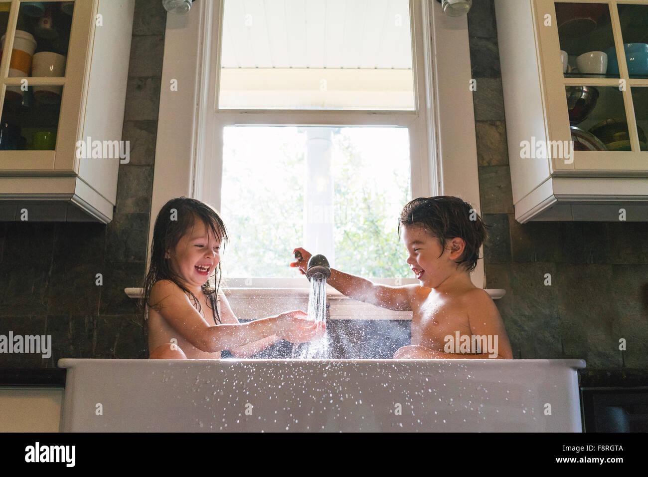 Chico y chica sentada en el lavabo de la cocina jugando con agua Foto de stock