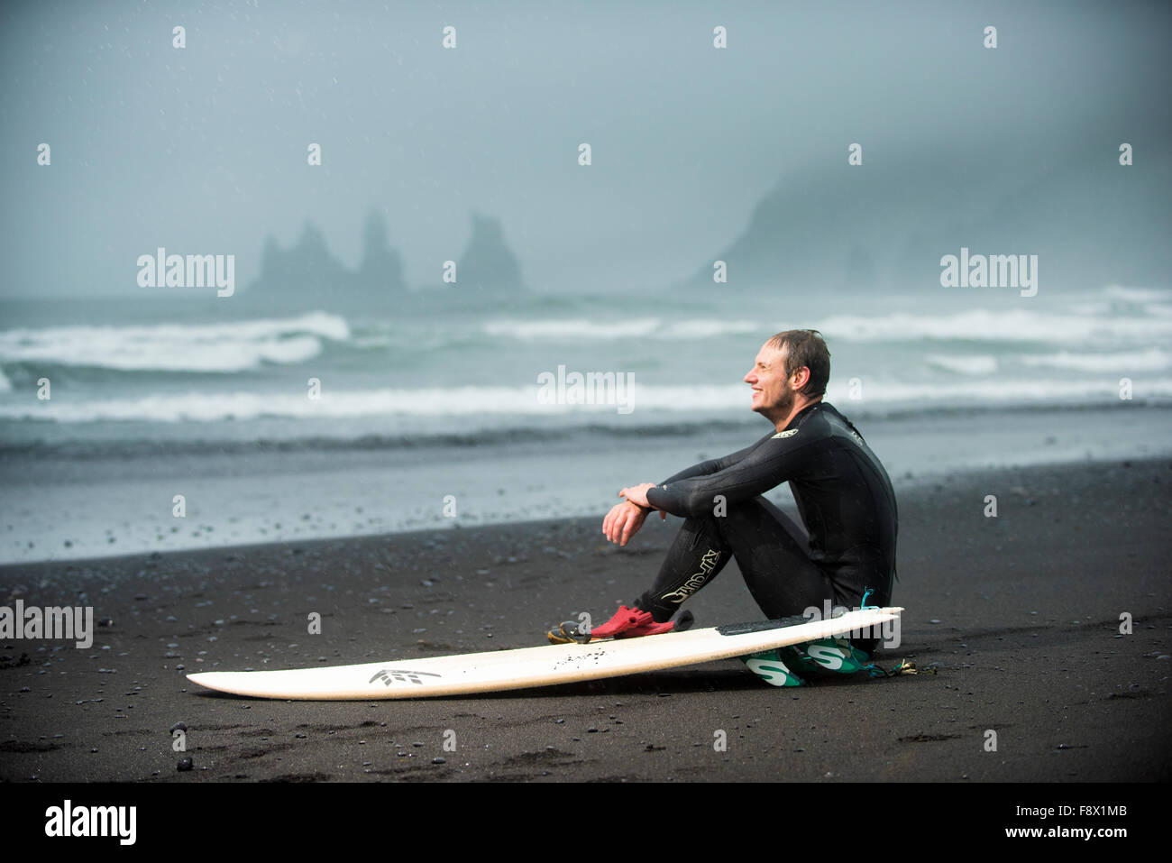 Fuera de Vik. Surfer sentado en la playa de arena negra para descansar. Foto de stock
